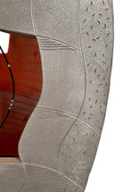 Carved, rib-like vertical lines cover the lower two-thirds of the form, with some sections resembling stacked bricks or tire treads. A subtle metallic silver finish catches the light on the right half, contrasting with the chalky finish on the left. The top third of the sculpture is a smooth, rounded cap. Rectangular cutouts on both sides pierce through the outer layer, revealing a hollow interior glowing with vibrant, airbrushed gradients of neon pink, orange, yellow, and green.