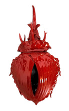 A vibrant, glossy red ceramic sculpture of a rhinoceros beetle by Enza Fasano. The piece features a highly reflective, deep crimson glaze that accentuates its smooth, rounded abdomen and the intricate, jagged textures of its head and horns.