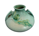 A squat, rounded vintage Roseville pottery vase in a light teal-blue matte glaze. The vase features two small, angular geometric handles on its shoulders and a flared rim. Embossed on the front is a cluster of textured, green and pale-yellow thornapple blossoms tucked against sharp, serrated green leaves. The surface shows a subtle, fine network of age-related crazing lines throughout the glaze.