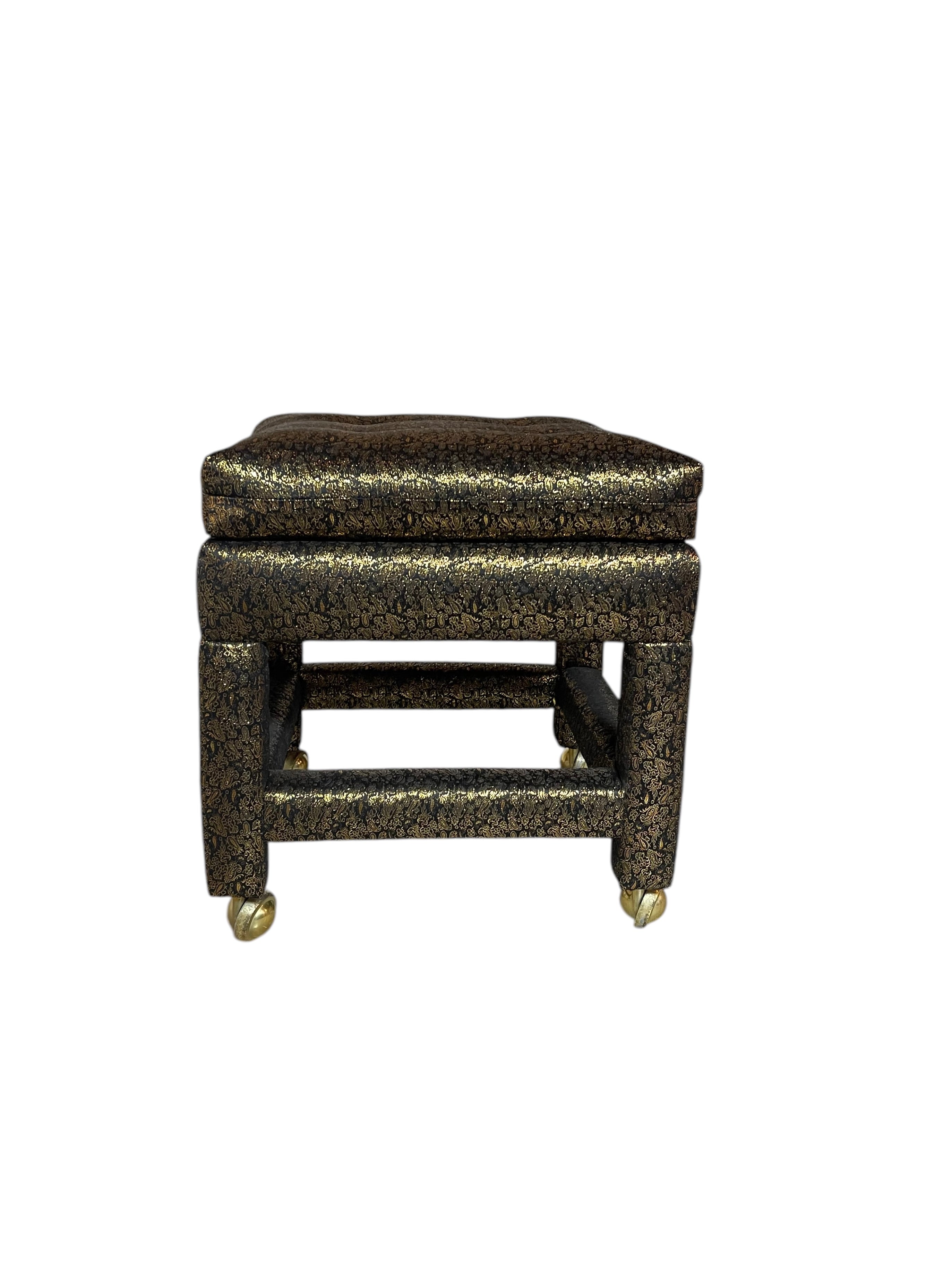 An upholstered, postmodern, square foot stool with a black and gold patterned silk, featuring a cushioned top and metal legs.