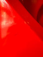 A top-down, straight-on view of a vintage, high-gloss cherry red bathtub. The tub basin is molded into a distinct double-tiered heart shape, with a shallower outer heart cascading into a deeper, smaller inner heart basin centered within a wide rectangular red deck.