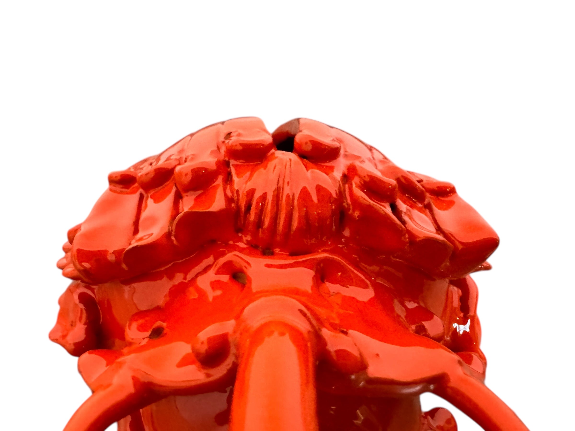 A glossy, vibrant orange ceramic sculpture of a rhinoceros beetle by Enza Fasano. The piece features a highly polished, reflective glaze and stylized, fluid anatomical details. Its prominent dual horns curve forward, and the body is textured with layered, wing-like plates, set against a plain white background.