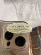 A large, decorative ceramic bowl by Dolbi Cashier in a dramatic Postmodern style. The top half is finished in a polished, piano-black glaze with an organic, wavy "butterfly" rim that dips in the center and rises at the sides. The bottom half is finished in a reflective, metallic silver chrome glaze, featuring bold, geometric-rounded feet and a structured base that appears to "hold" the black vessel. The overall shape is wide and sculptural, reminiscent of 1980s Art Deco Revival.