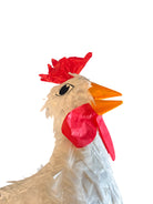 A white chicken pinata with red comb and wattles, and orange beak and legs, standing upright.