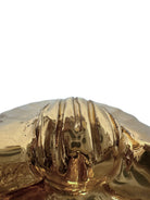 A handcrafted ceramic sculpture of a rhinoceros beetle by Enza Fasano, featuring a brilliant, high-gloss gold metallic finish. The beetle is captured in a dynamic, slightly upturned pose with detailed textures on its ribbed shell and prominent, curved horns. The piece reflects light across its polished surface, showcasing the artist’s signature fusion of traditional Pugliese pottery and contemporary luxury.