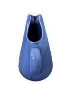 A Russel Wright American Modern stoneware water pitcher in a glossy Manitoga blue glaze is centered against a white background. The pitcher has a teardrop shape, a large handle, and a wide spout