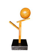 A wooden sculpture featuring a dark square base, a vertical trunk that branches into two angled supports, and a turned wooden sphere resting on the higher support.