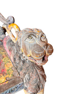 A pair of antique, heavily carved Anglo-Indian style throne chairs featuring lion figures as legs and arm supports, and peacock motifs on the backrests. The chairs have a distressed, multi-colored painted finish.