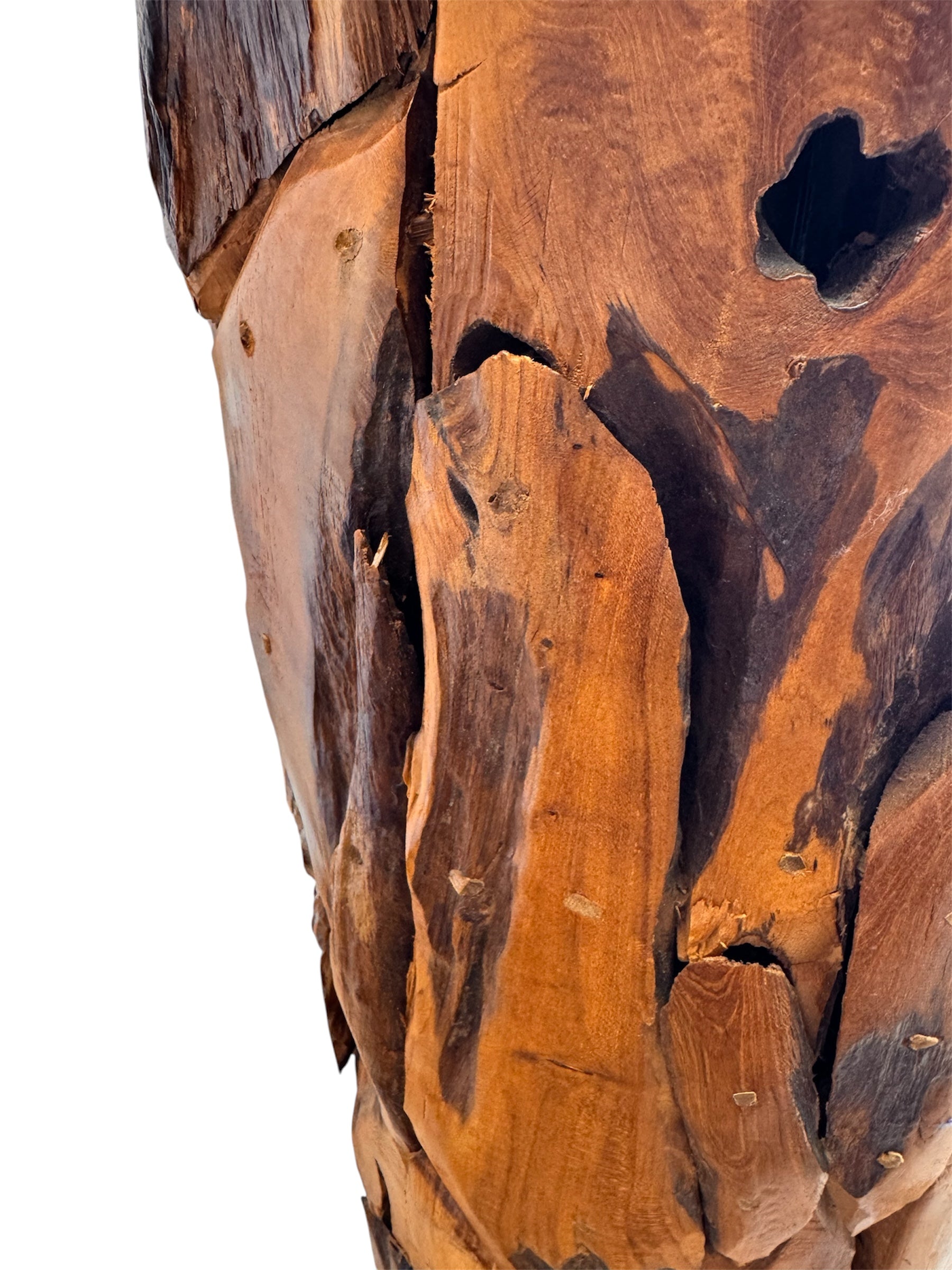 Two table lamps made from repurposed teak wood vases. The bases are tall and tapered, featuring a rugged, mosaic-like texture composed of various pieces of dark, polished teak wood with visible natural grain and crevices. Each lamp is topped with a large, warm-toned conical shade that is currently wrapped in protective clear plastic, emitting a soft, golden glow. The lamps are positioned on a clean white surface against a neutral background.
