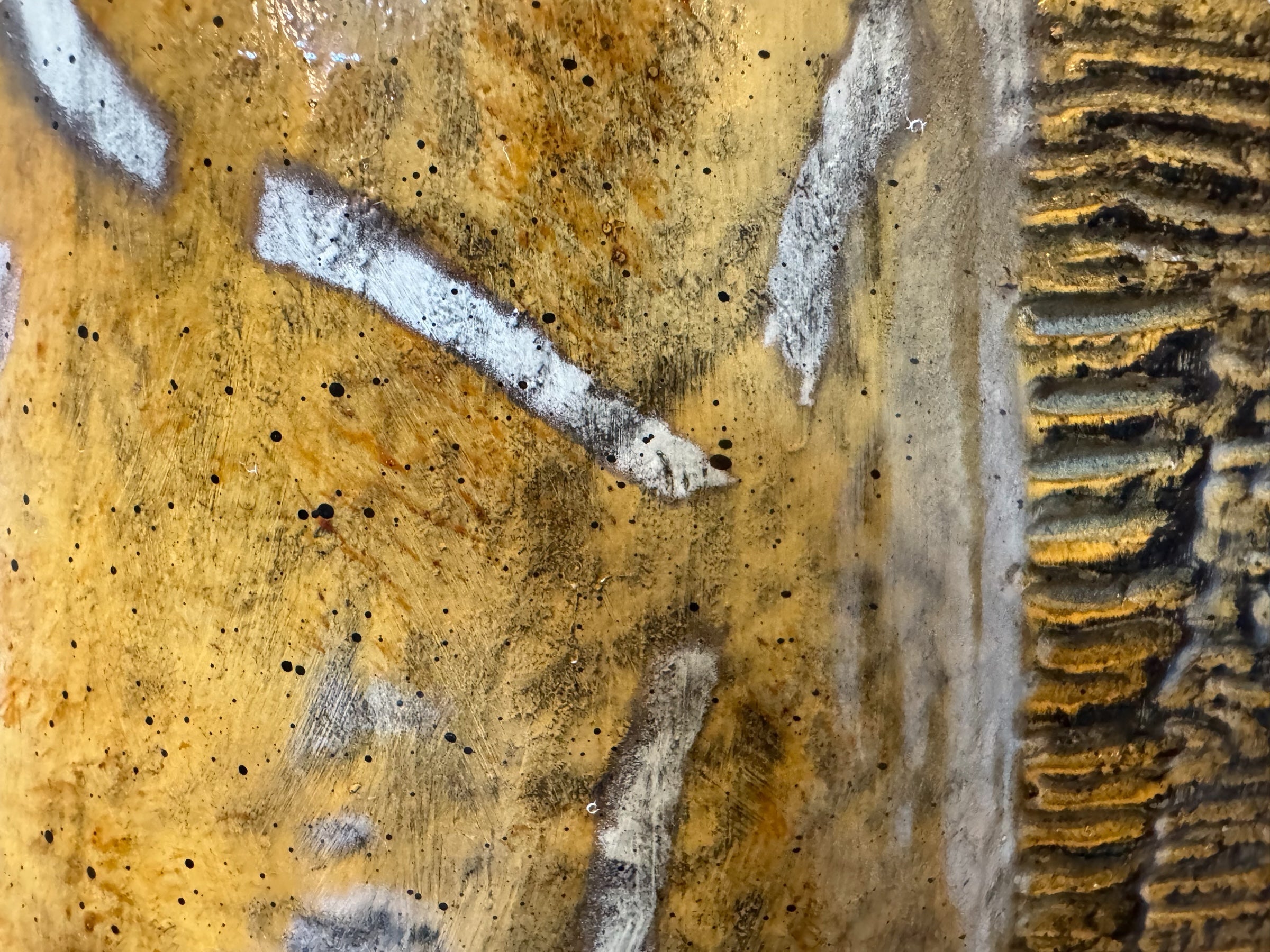 A hand-painted, cast resin sculpture of a seated giraffe. The giraffe has a long neck, is predominantly gold with light markings, and is in a resting pose. The sculpture is against a plain white background