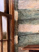 A realistic painting of a rustic interior scene by Travis Whitfield. A duck sits inside a woven basket on a dark wooden table with a single drawer. A French horn hangs on the light blue and white log wall behind the table. A multi-pane window on the left side of the painting shows an outdoor view. 