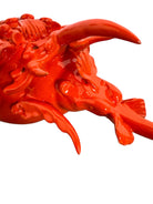 A glossy, vibrant orange ceramic sculpture of a rhinoceros beetle by Enza Fasano. The piece features a highly polished, reflective glaze and stylized, fluid anatomical details. Its prominent dual horns curve forward, and the body is textured with layered, wing-like plates, set against a plain white background.