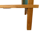 A three-tiered wooden shelving unit featuring a mix of light oak and teal-colored panels. The piece has an open, structural design with visible joinery, vertical supports that extend past the top shelf, and a horizontal backrest at the top. The middle and bottom shelves feature slatted wood center sections flanked by solid teal panels, while the top surface is primarily solid wood with teal accents at the edges.