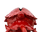A vibrant, glossy red ceramic sculpture of a rhinoceros beetle by Enza Fasano. The piece features a highly reflective, deep crimson glaze that accentuates its smooth, rounded abdomen and the intricate, jagged textures of its head and horns.