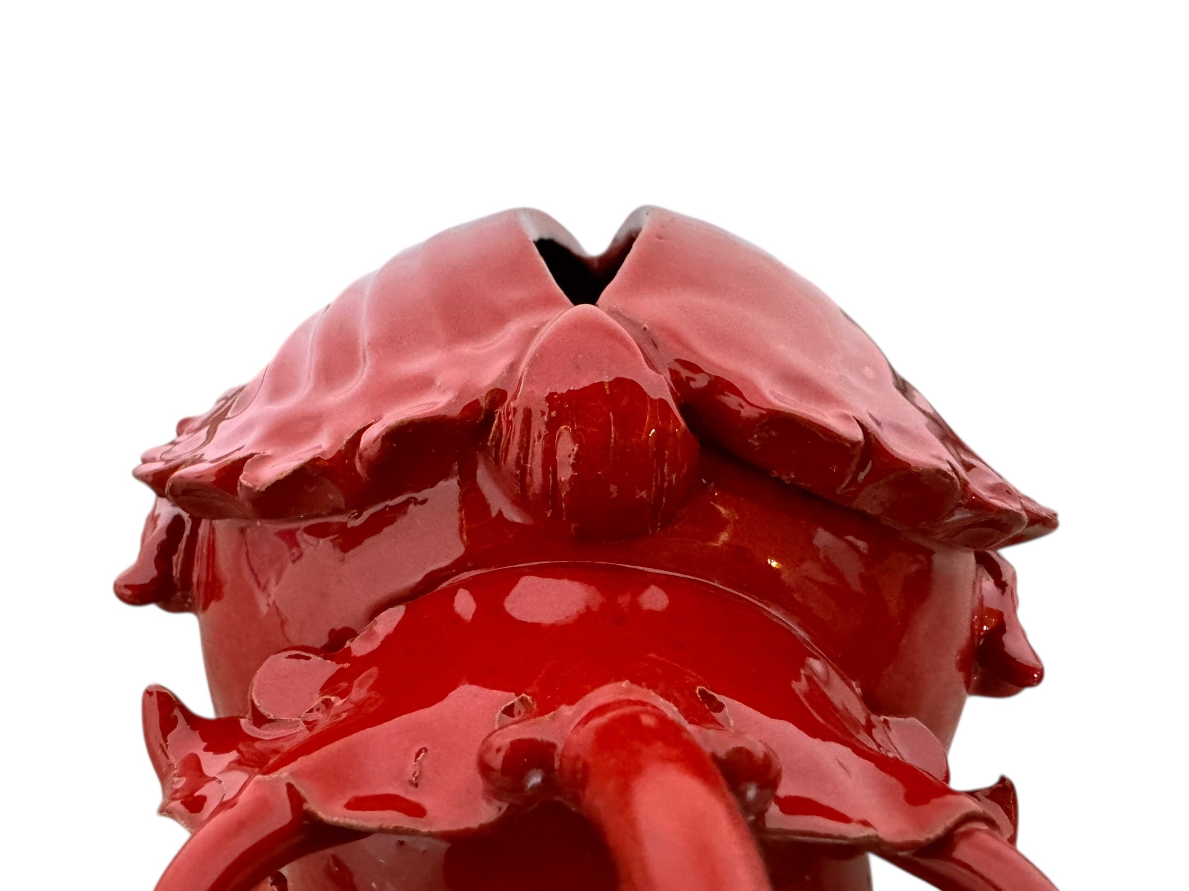 A vibrant, glossy red ceramic sculpture of a rhinoceros beetle by Enza Fasano. The piece features a highly reflective, deep crimson glaze that accentuates its smooth, rounded abdomen and the intricate, jagged textures of its head and horns.