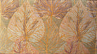 A Neoclassical-style wooden loveseat with a dark mahogany frame featuring scrolled arms and tapered legs. The upholstery consists of plush cushions and two matching cylindrical bolster pillows, all covered in a golden-yellow jacquard fabric with a large-scale, repeating autumnal leaf pattern in shades of muted orange and brown.