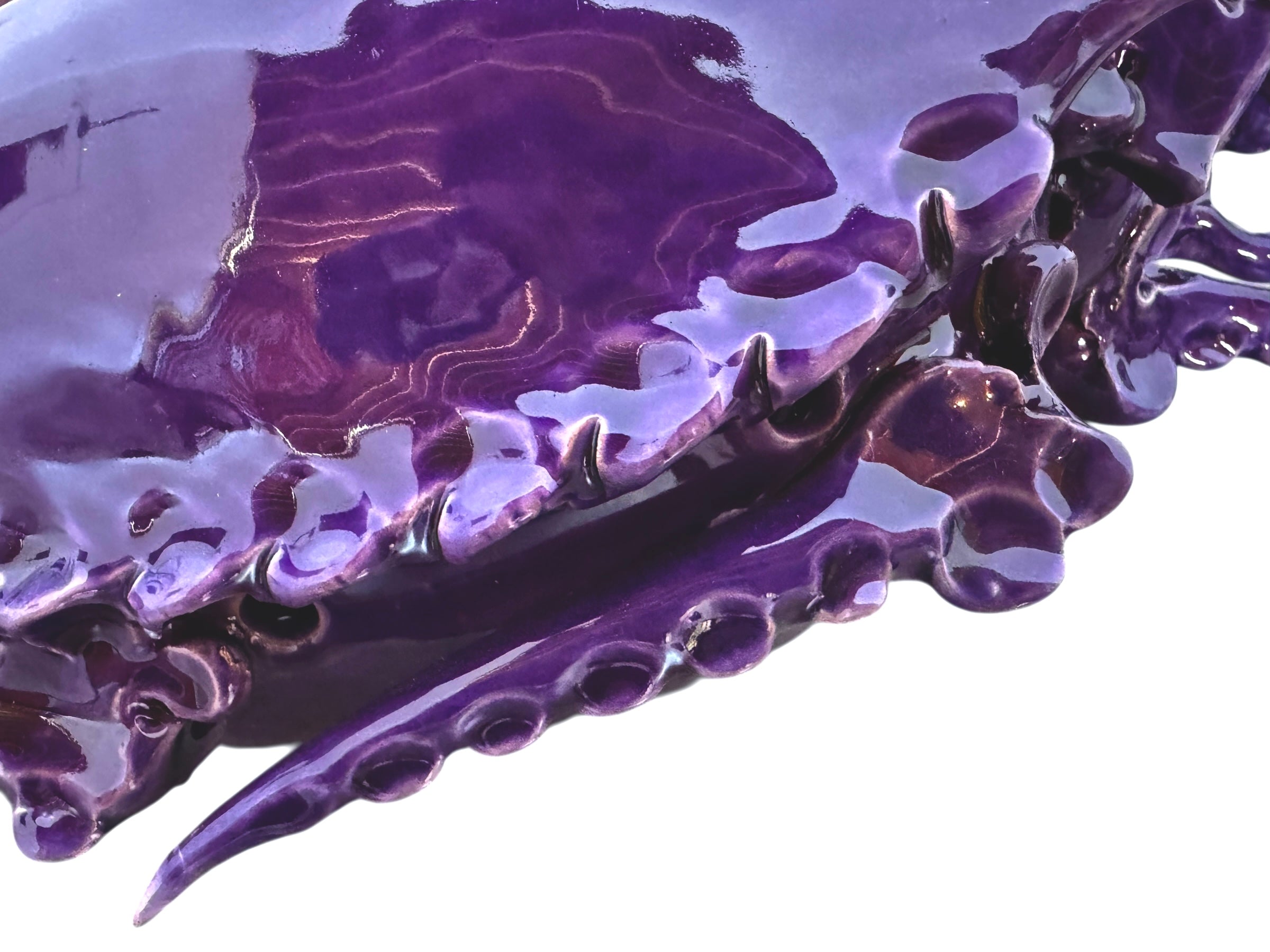 A glossy, deep purple ceramic sculpture of a beetle by Enza Fasano. The piece features a highly stylized and ornate design, blending insect-like anatomy with fantastical elements. It has a smooth, rounded shell and elongated, curved mandibles and appendages lined with sharp, thorn-like protrusions. The monochromatic glaze is reflective, highlighting the intricate sculptural details and textures of the avant-garde artwork.