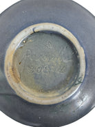 A squat, rounded vintage Roseville pottery vase in a light teal-blue matte glaze. The vase features two small, angular geometric handles on its shoulders and a flared rim. Embossed on the front is a cluster of textured, green and pale-yellow thornapple blossoms tucked against sharp, serrated green leaves. The surface shows a subtle, fine network of age-related crazing lines throughout the glaze.