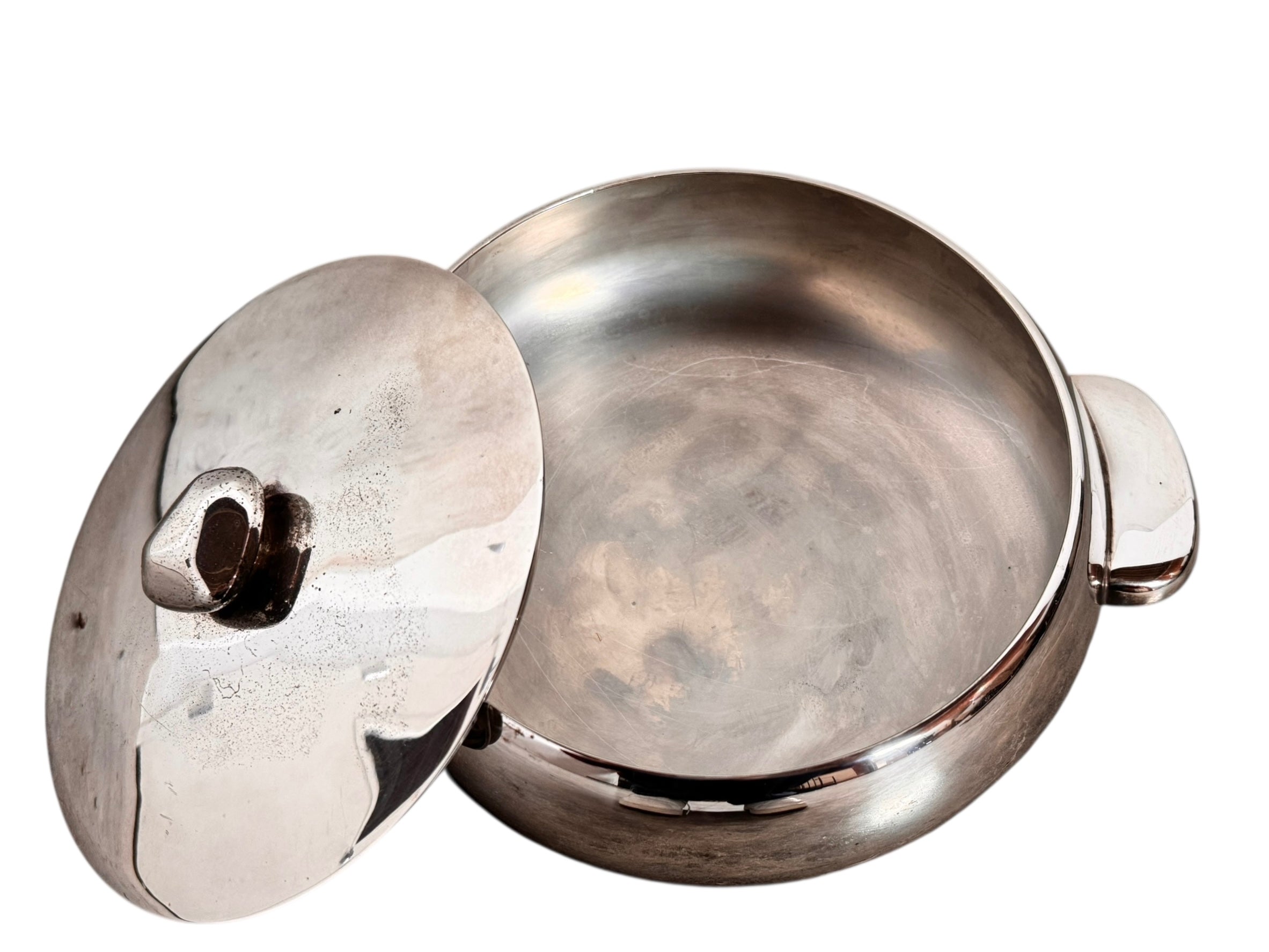 Round St. James silver-plated lidded serving dish from the 1980s, featuring a minimalist modernist design with geometric side handles and a sculptural, biomorphic finial, showing visible vintage wear and pitting on the metallic surface.