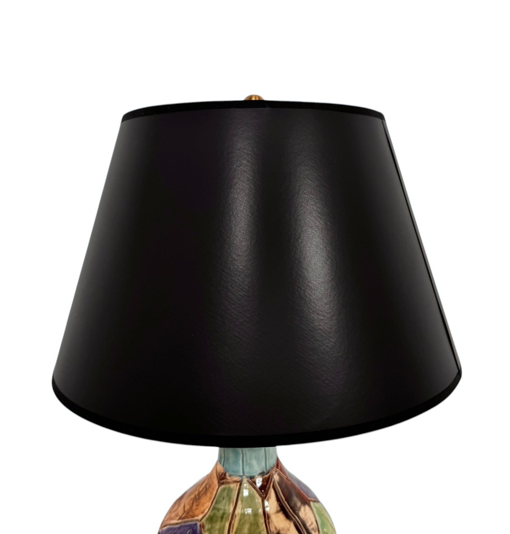 A hand-crafted ceramic table lamp featuring a vibrant, multi-colored base and a sleek black shade. The base is an upcycled artisan vase with a textured, hand-thrown appearance, decorated with geometric panels in shades of mustard yellow, forest green, cobalt blue, and burgundy, separated by thick black outlines. The lamp is topped with a minimalist, black tapered drum shade that provides a sharp contrast to the colorful, eclectic pottery below.

