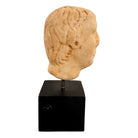 An ancient marble sculpted head of a young man, presented on a modern black presentation stand. The sculpture is rendered in a three-quarter view, angled slightly to the right, showing a classical profile characterized by a strong nose, softly contoured cheekbones, and slightly parted lips that convey a quiet, contemplative expression. The hair is carved in short, stylized strands that frame the forehead and ears, characteristic of ancient Roman or Greek portraiture styles.