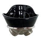 A large, decorative ceramic bowl by Dolbi Cashier in a dramatic Postmodern style. The top half is finished in a polished, piano-black glaze with an organic, wavy "butterfly" rim that dips in the center and rises at the sides. The bottom half is finished in a reflective, metallic silver chrome glaze, featuring bold, geometric-rounded feet and a structured base that appears to "hold" the black vessel. The overall shape is wide and sculptural, reminiscent of 1980s Art Deco Revival.