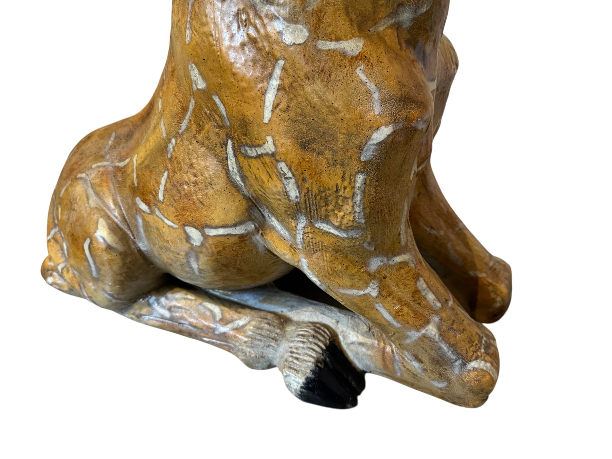 A hand-painted, cast resin sculpture of a seated giraffe. The giraffe has a long neck, is predominantly gold with light markings, and is in a resting pose. The sculpture is against a plain white background