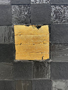 A triptych of abstract paintings featuring a grid pattern of textured black squares by Sabine Stromeyer called “Square One”. The left and right panels each have a single vertical gold rectangle in the center, while the middle panel has two stacked gold rectangles in the center.