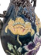 An ornate, dark glazed ceramic Art Nouveau vase with two handles and raised floral designs in yellow, purple, and green.