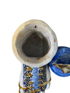 Close-up of a ceramic foot sculpture by Domenico Pinto. The foot is decorated with intricate hand-painted designs inspired by Apulian folklore and accented with 24KT gold. A stylized gilt mask sits atop the foot.