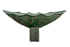 curved ceramic piece resembling a green pod, supported by a block plinth. The seafoam-green ceramic structure extends wide on either side, curving upward to form a wavy, boat-like shape. The outer surface is dotted with rows of small, raised, brown-orange, acorn-like protrusions. The top rim is layered with parallel, grooved ridges. The base is a vertical rectangular block with a heavily textured, bark-like surface in a dark green and black finish.