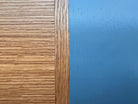 A three-tiered wooden shelving unit featuring a mix of light oak and teal-colored panels. The piece has an open, structural design with visible joinery, vertical supports that extend past the top shelf, and a horizontal backrest at the top. The middle and bottom shelves feature slatted wood center sections flanked by solid teal panels, while the top surface is primarily solid wood with teal accents at the edges.