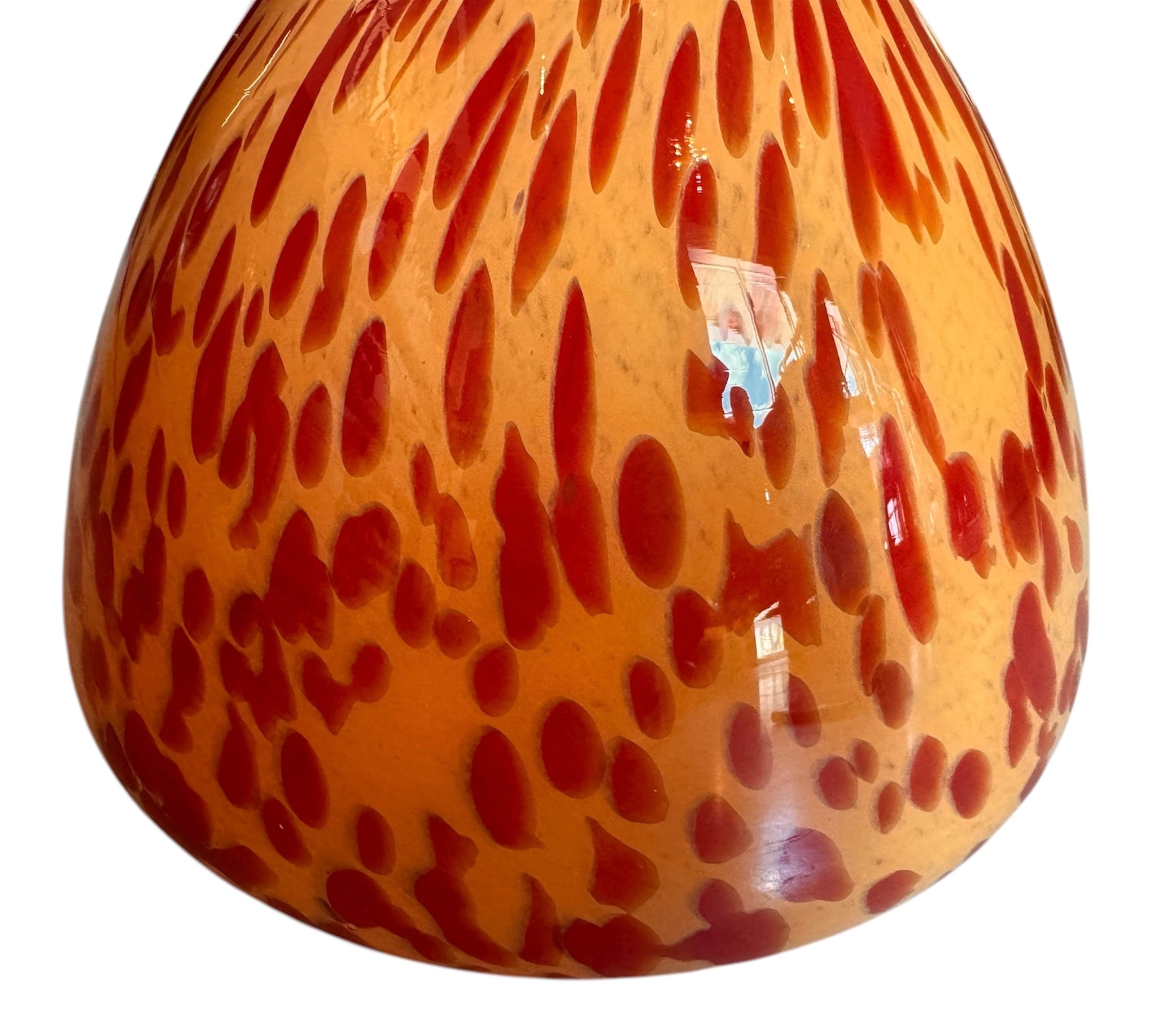 A hand-blown Italian Murano glass vase featuring a wide, bulbous body and a short, flared rim. The glass is a vibrant, translucent amber-orange base decorated with an organic "macchia" or spotted pattern of deep ruby red blotches. The red spots are elongated and vertical near the neck, becoming larger and more rounded toward the base. The surface has a high-gloss, reflective finish, showcasing mid-century modern craftsmanship.
