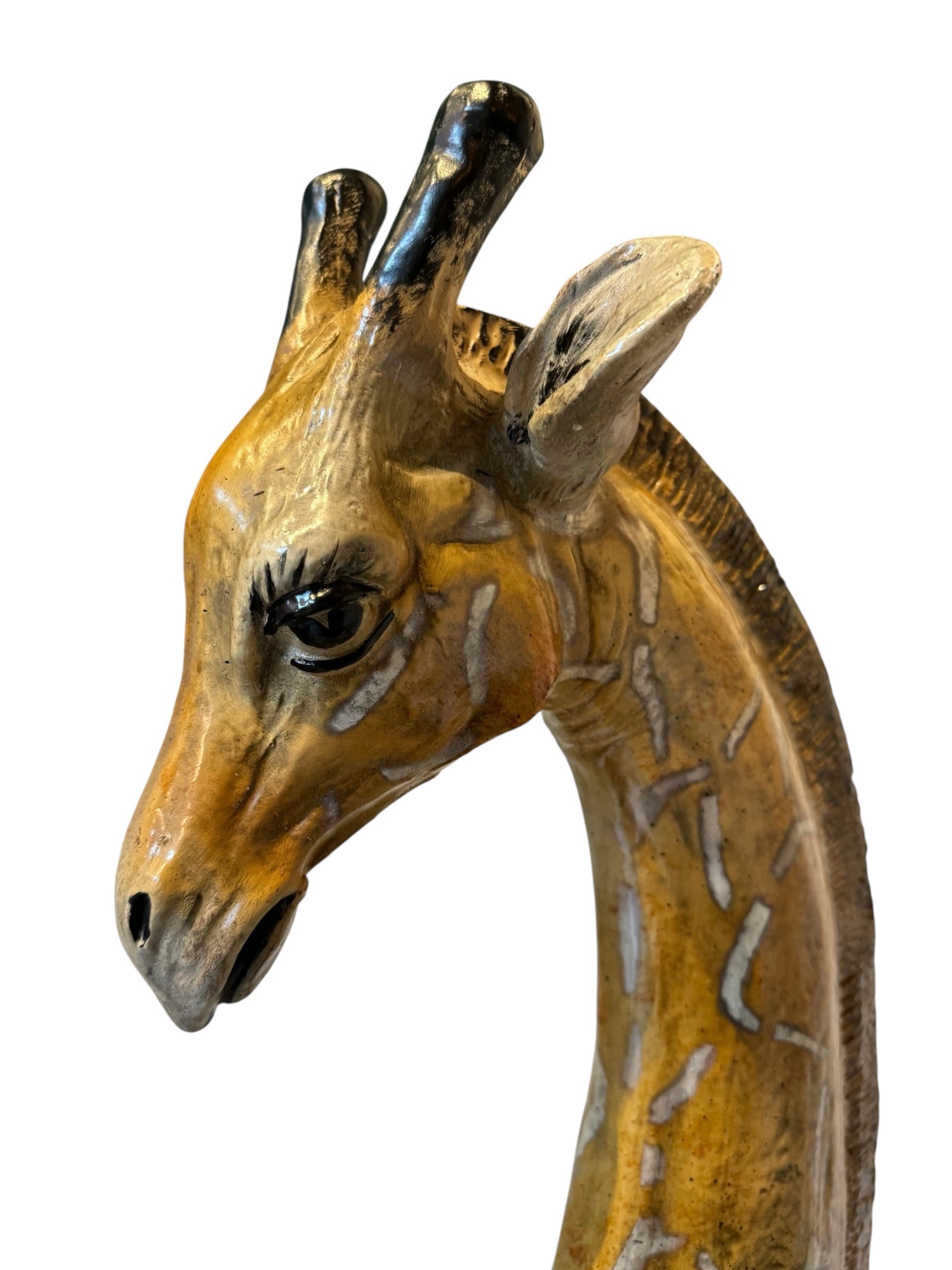 A hand-painted, cast resin sculpture of a seated giraffe. The giraffe has a long neck, is predominantly gold with light markings, and is in a resting pose. The sculpture is against a plain white background