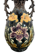 An ornate, dark glazed ceramic Art Nouveau vase with two handles and raised floral designs in yellow, purple, and green.