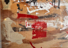 horizontal rectangular mixed media abstract artwork by J. Rogers, dated 2010, presented in a thin black frame. The composition is set against a light-toned wood grain background and features a dynamic, gestural arrangement of thick white impasto, splatters of red and black paint, and aggressive black scribbles. A vertical strip of textured material is collaged near the center, while various washes of tan and cream create a sense of weathered depth across the wooden surface.