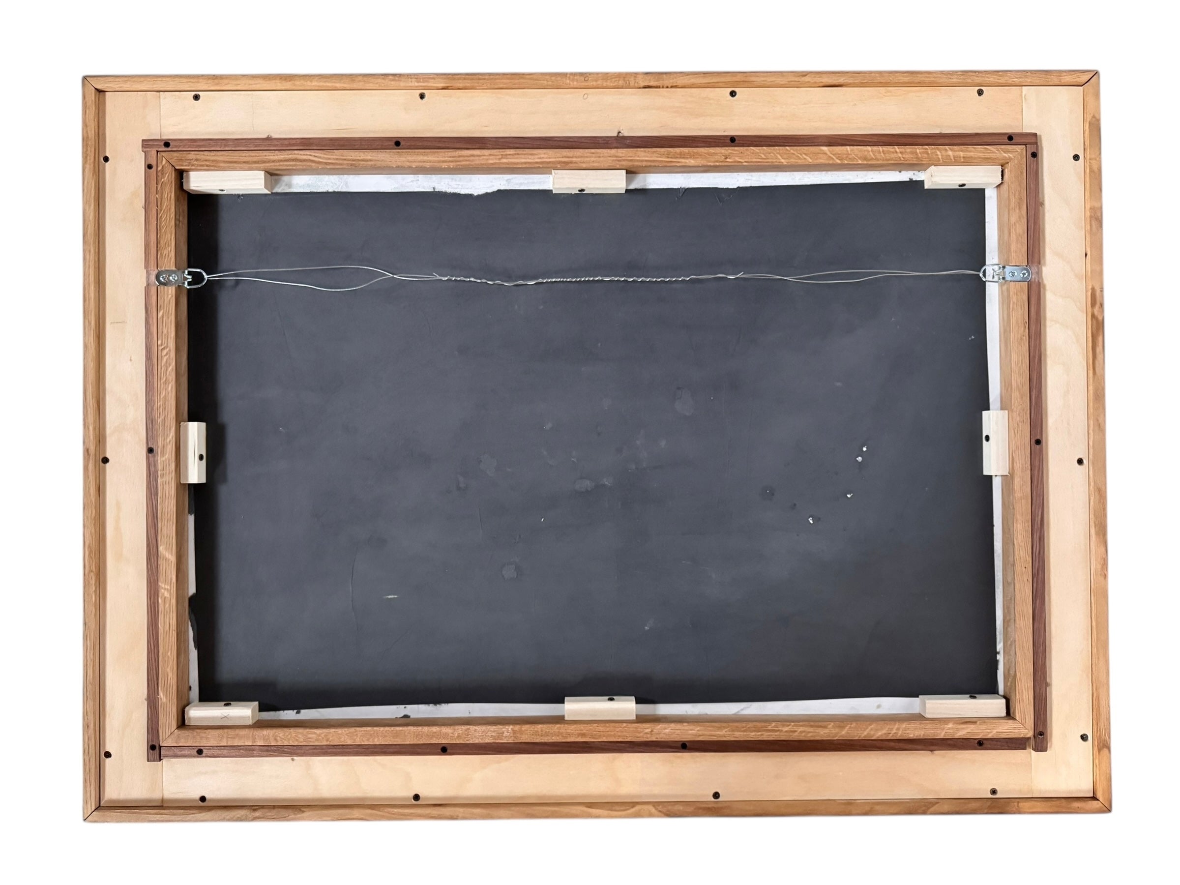 A vibrantly colored landscape painting titled 'Perdernales Falls Fisherman,' featuring two large trees with prominent exposed roots framing a body of water. A lone figure, a fisherman, stands by the water in the middle ground. The painting uses bold strokes of yellow, green, red, and blue, and is enclosed in a rustic dark wooden frame with a light-colored inner mat.