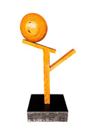 A wooden sculpture featuring a dark square base, a vertical trunk that branches into two angled supports, and a turned wooden sphere resting on the higher support.