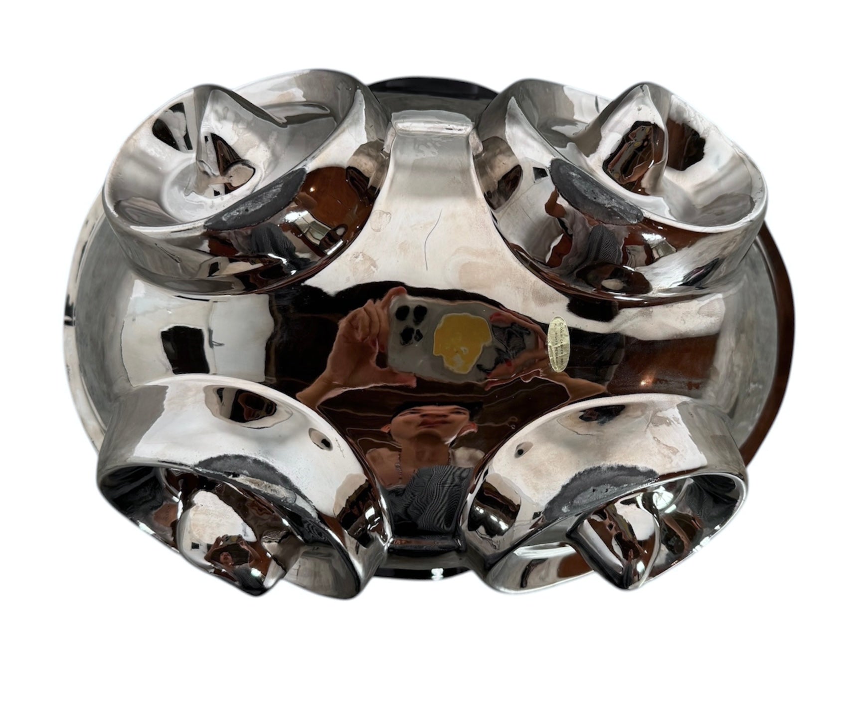 A large, decorative ceramic bowl by Dolbi Cashier in a dramatic Postmodern style. The top half is finished in a polished, piano-black glaze with an organic, wavy "butterfly" rim that dips in the center and rises at the sides. The bottom half is finished in a reflective, metallic silver chrome glaze, featuring bold, geometric-rounded feet and a structured base that appears to "hold" the black vessel. The overall shape is wide and sculptural, reminiscent of 1980s Art Deco Revival.