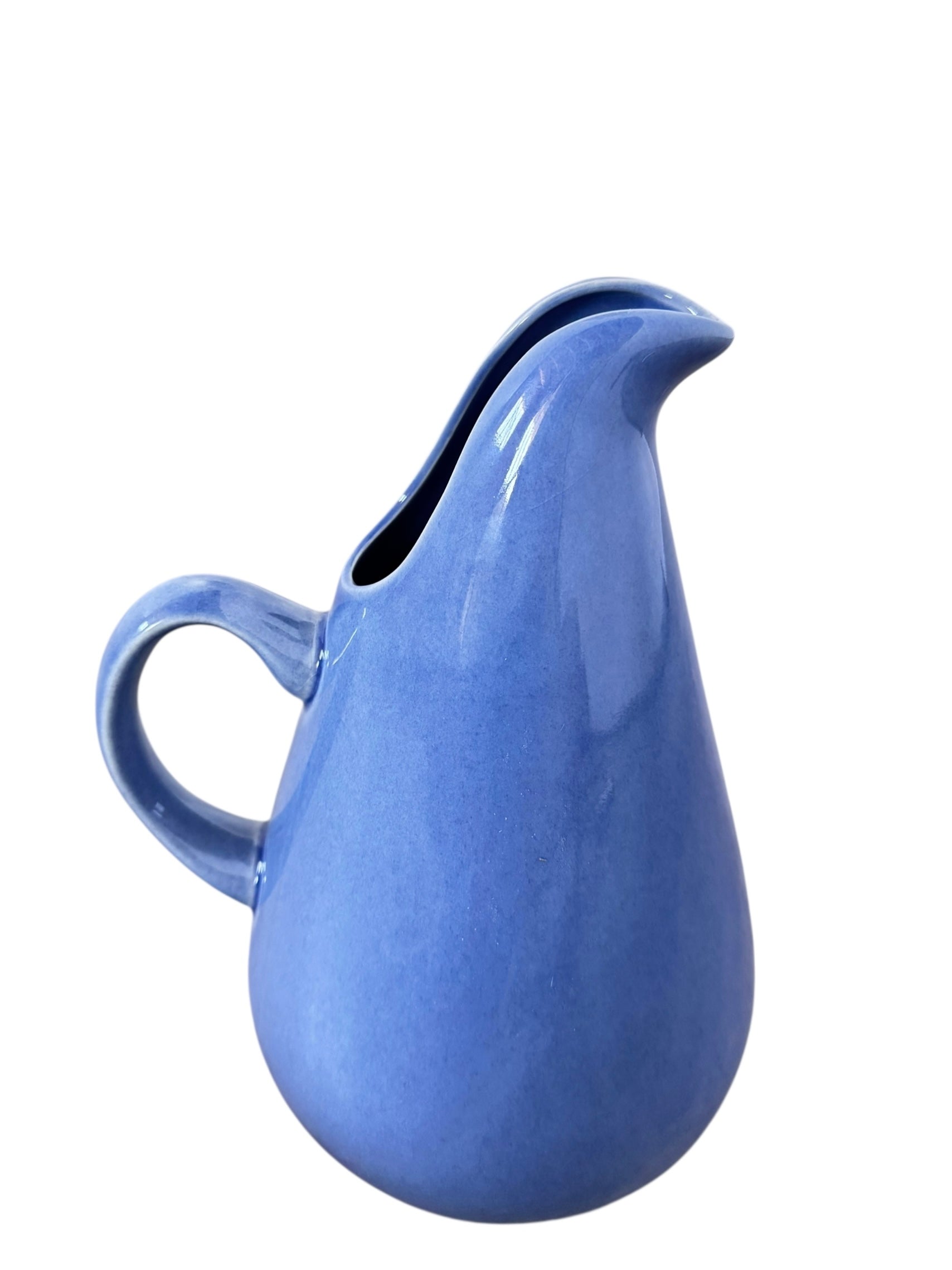 A Russel Wright American Modern stoneware water pitcher in a glossy Manitoga blue glaze is centered against a white background. The pitcher has a teardrop shape, a large handle, and a wide spout