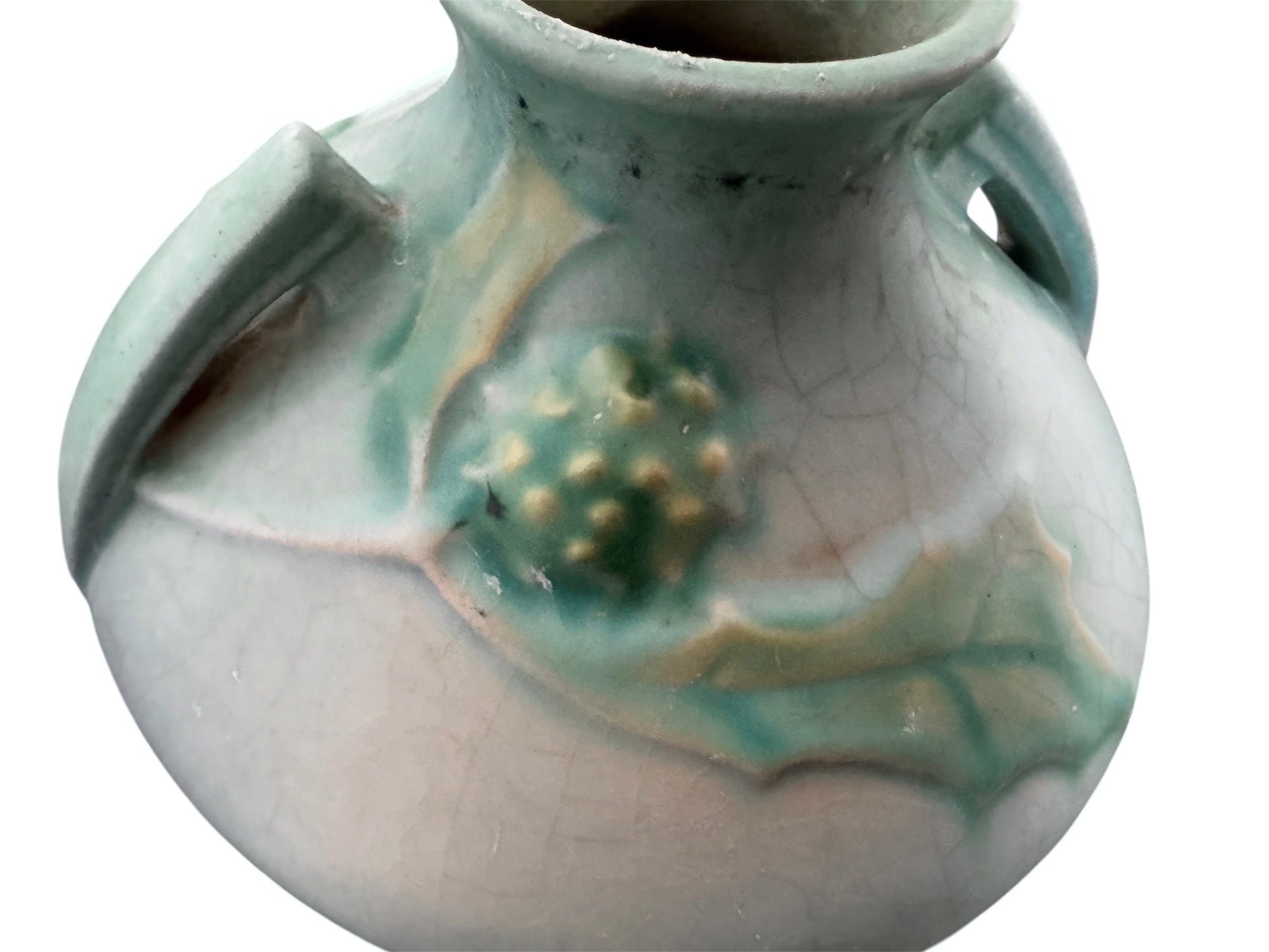A squat, rounded vintage Roseville pottery vase in a light teal-blue matte glaze. The vase features two small, angular geometric handles on its shoulders and a flared rim. Embossed on the front is a cluster of textured, green and pale-yellow thornapple blossoms tucked against sharp, serrated green leaves. The surface shows a subtle, fine network of age-related crazing lines throughout the glaze.