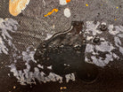 An abstract, vertical-oriented canvas painting featuring a dark background layered with highly textured, horizontal bands. The composition alternates between solid black strips and dense, speckled white-and-grey patterns that resemble static or stone texture. Splattered across the surface are energetic drips, lines, and splotches of bright yellow, stark white, and grey paint, creating a chaotic yet rhythmic sense of movement overlaying the geometric structure underneath.