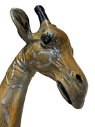 A hand-painted, cast resin sculpture of a seated giraffe. The giraffe has a long neck, is predominantly gold with light markings, and is in a resting pose. The sculpture is against a plain white background