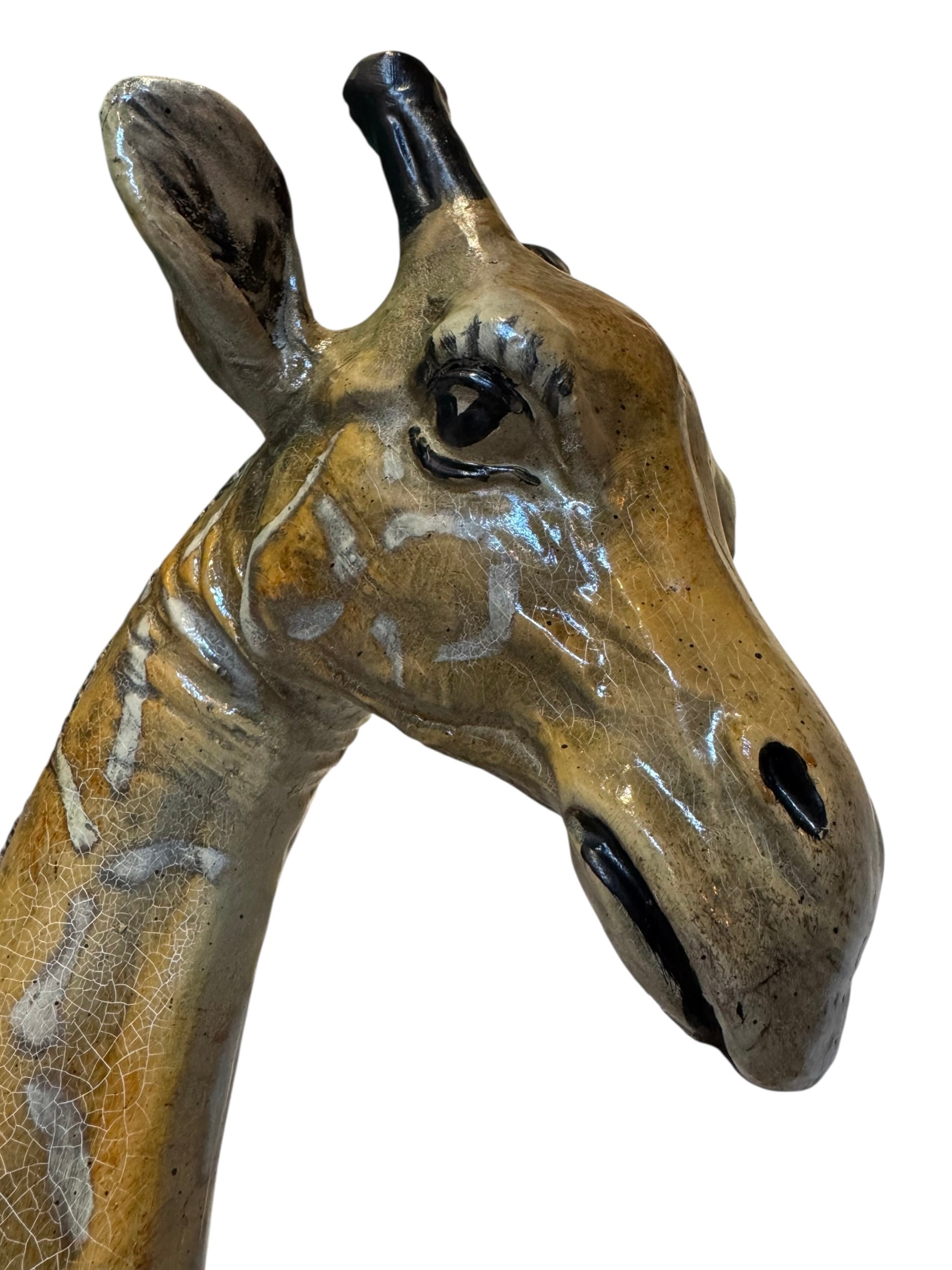 A hand-painted, cast resin sculpture of a seated giraffe. The giraffe has a long neck, is predominantly gold with light markings, and is in a resting pose. The sculpture is against a plain white background