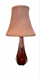A table lamp featuring a teardrop-shaped, reddish-purple glass base and a conical, pleated, light-pink fabric shade.