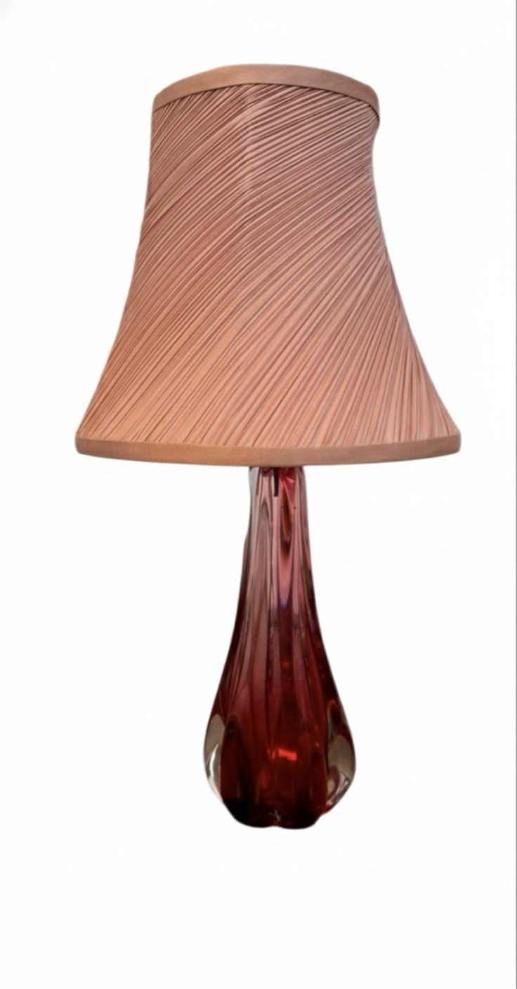 A table lamp featuring a teardrop-shaped, reddish-purple glass base and a conical, pleated, light-pink fabric shade.