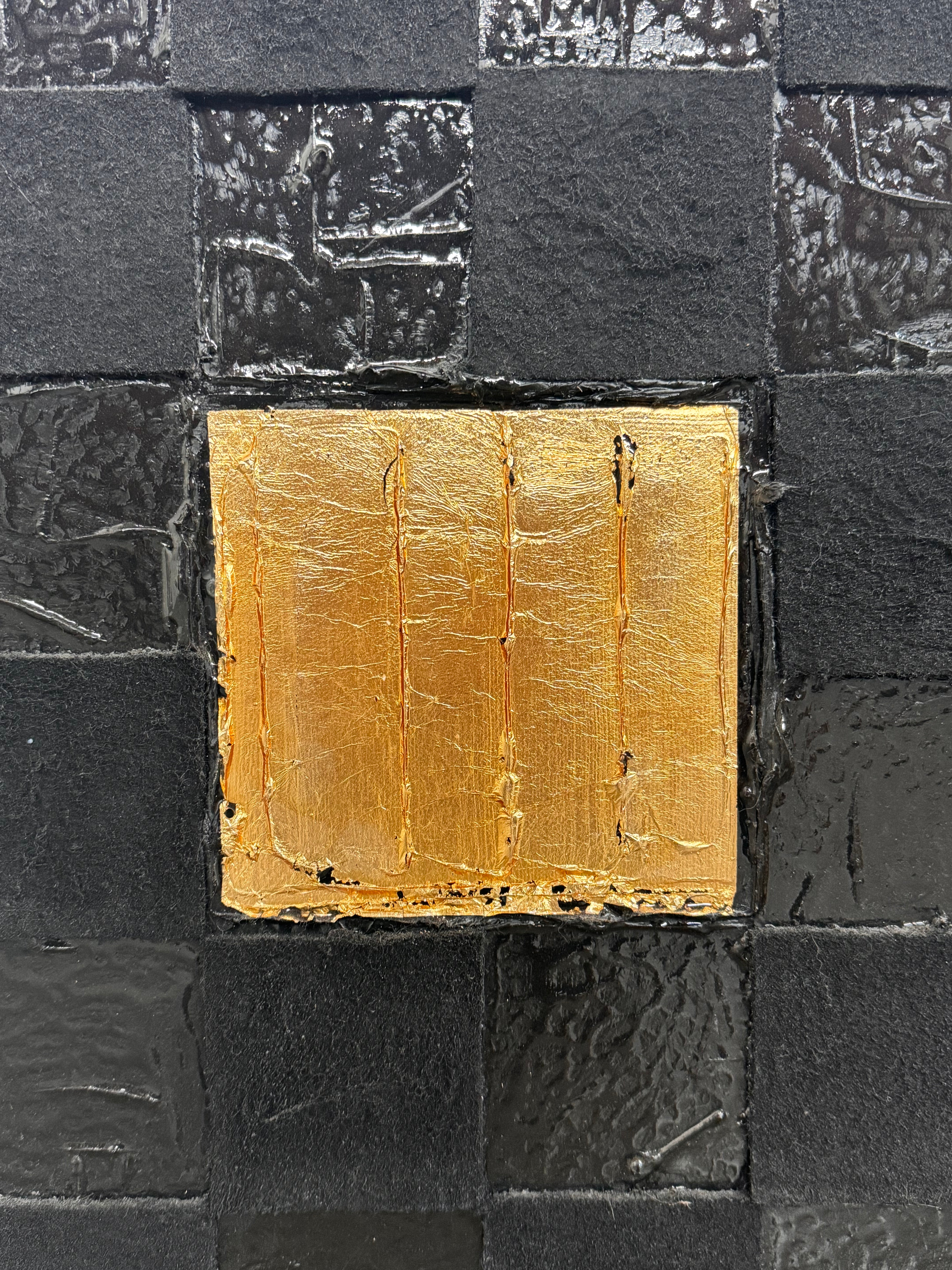 A triptych of abstract paintings featuring a grid pattern of textured black squares by Sabine Stromeyer called “Square One”. The left and right panels each have a single vertical gold rectangle in the center, while the middle panel has two stacked gold rectangles in the center.