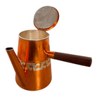The set includes a large, rectangular, hammered copper tray with geometric openwork handles. Resting on the tray is a tall, slightly tapered copper coffee pot with a wooden handle, a matching smaller creamer pitcher with a similar wooden handle, a lidded sugar bowl, and a tiny matching metal cup or jigger. To the right off the tray sits a large, spherical copper water pitcher or jug with a wide mouth and ice lip.