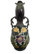 An ornate, dark glazed ceramic Art Nouveau vase with two handles and raised floral designs in yellow, purple, and green.