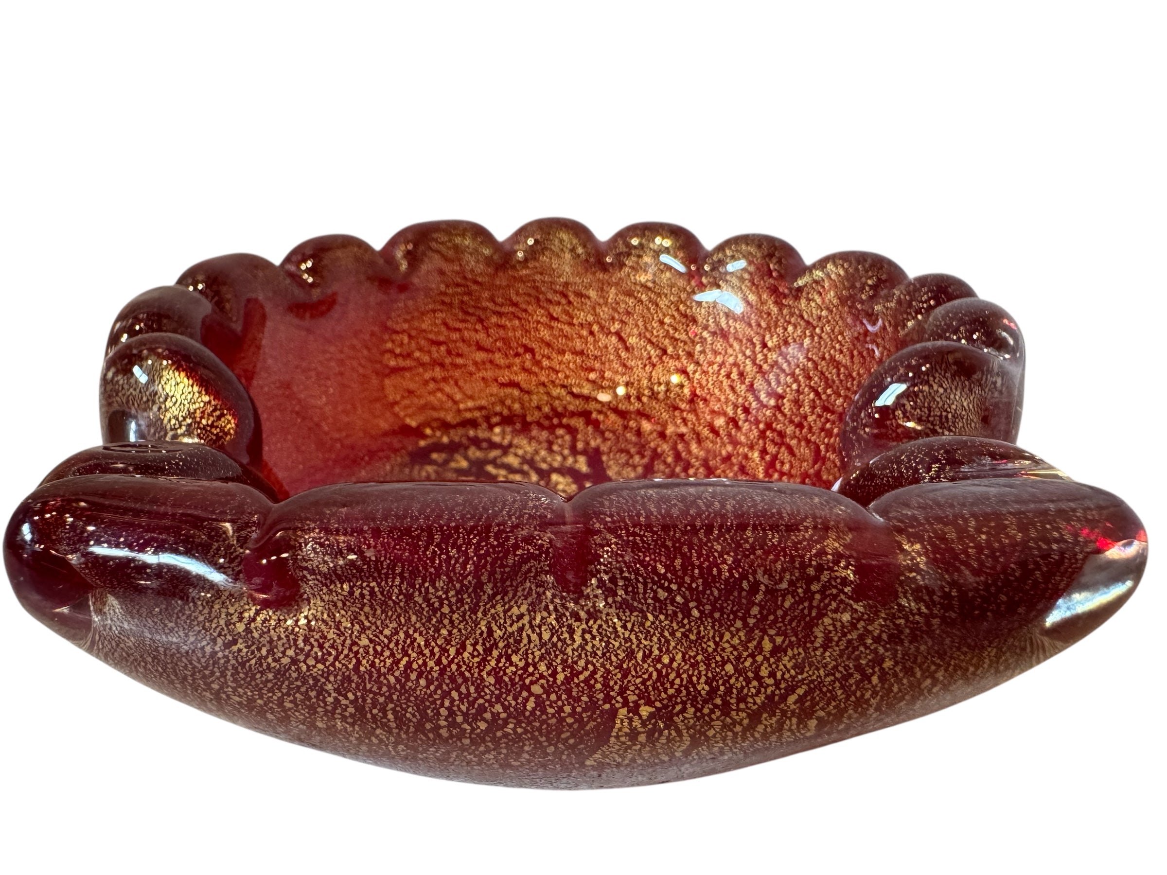 A handcrafted Murano glass bowl with a ruffled edge, deep red color, and gold specks created using the "oro zecchino" technique. The surface has a crackled gold pattern that reflects light, making it a striking decorative piece.